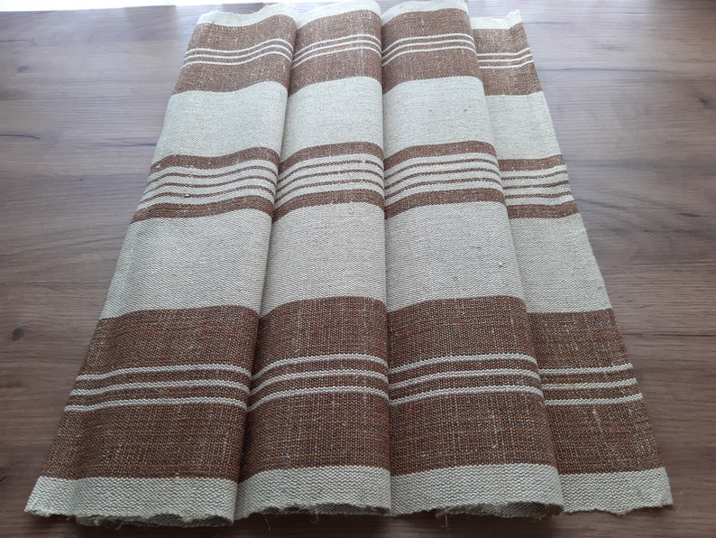 May include: Four brown and white striped linen tea towels. The towels are folded and laid out on a wooden surface.
