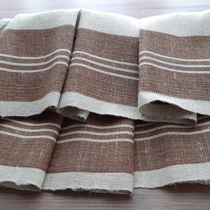 May include: A set of four brown and white striped linen tea towels. The towels are folded and arranged in a fan shape.