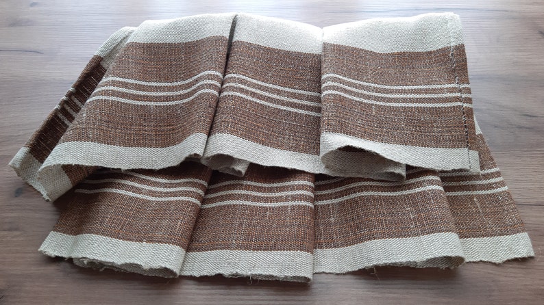 May include: A set of four brown and white striped linen tea towels. The towels are folded and arranged in a fan shape.
