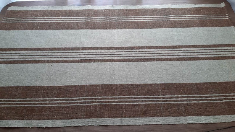 May include: A brown and beige striped fabric with a woven texture. The fabric has a subtle sheen and is perfect for a variety of home decor projects.