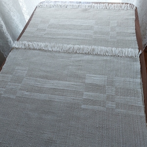 May include: A close-up of a white woven table runner with a fringe border. The runner has a subtle geometric pattern.