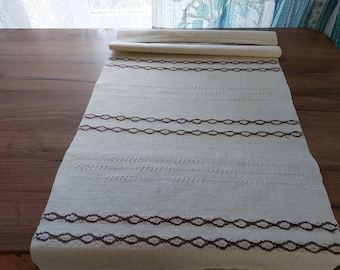 May include: A white linen table runner with a brown geometric pattern. The runner is folded in half and has a simple, rustic design.