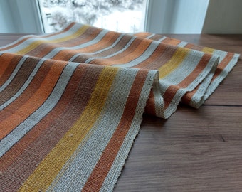 May include: A striped fabric runner in shades of orange, brown, and beige. The runner is woven with a textured pattern and has a natural, rustic look.