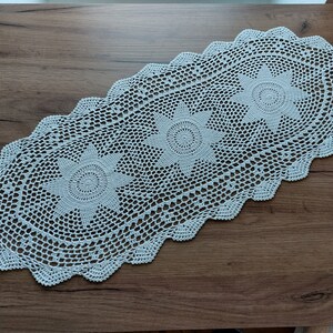May include: White crocheted table runner with a scalloped edge and three floral designs.