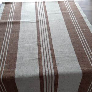 May include: A brown and white striped table runner. The runner is made of a woven fabric and has a rustic look.