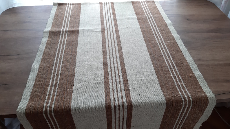 May include: A brown and white striped table runner. The runner is made of a woven fabric and has a rustic look.
