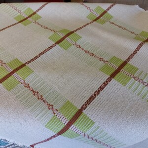 May include: A white woven throw blanket with a green and brown plaid pattern.
