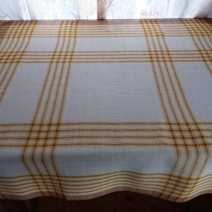 May include: A white tablecloth with a brown and yellow plaid pattern. The tablecloth is made of a woven fabric and has a slightly textured surface.