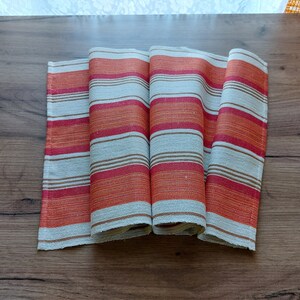 May include: A set of four folded kitchen towels with a striped pattern in orange, red, and white.