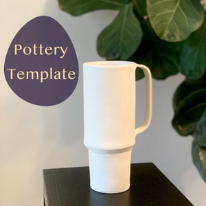 May include: White ceramic mug with a handle and a band around the middle. The mug is sitting on a black surface.