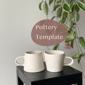 以下が含まれることがあります： 黒い木製の台の上に置かれた、白い陶器製のマグカップ2つ。マグカップはサイズと形が異なります。背景は白い壁で、緑の植物があります。