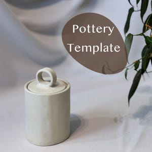 Puede incluir: Un tarro cilíndrico de cerámica blanquecina con tapa y asa de bucle. El tarro está sobre una superficie blanca con un fondo suave y neutro. El texto "Pottery Template" está en forma ovalada marrón.