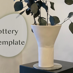 May include: A white ceramic vase with a wide, flared opening and a cylindrical base. The vase is sitting on a black surface with a gray circular coaster. The vase is empty and has a smooth, matte finish. The text "Pottery Template" is visible in the image.