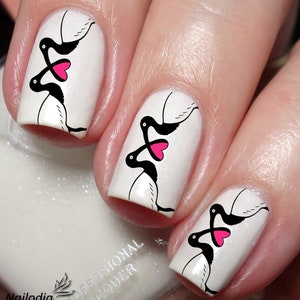 May include: Close-up of fingernails with white polish and black and pink nail art featuring a design of two birds with hearts. The nail art is a Valentine's Day theme.
