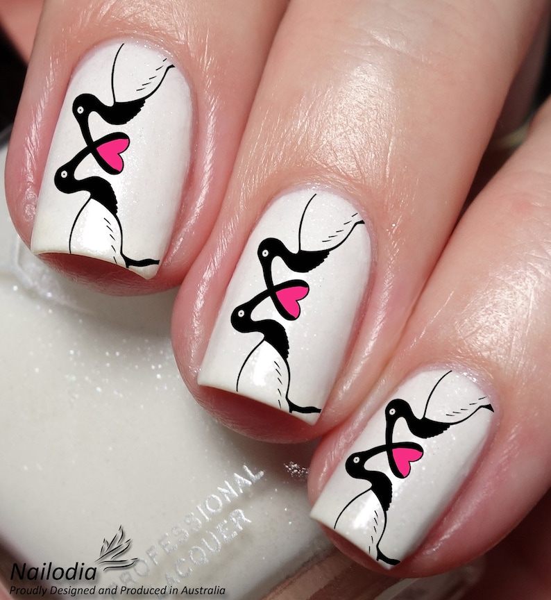 May include: Close-up of fingernails with white polish and black and pink nail art featuring a design of two birds with hearts. The nail art is a Valentine's Day theme.