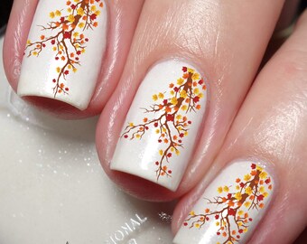 May include: White nail polish with fall-themed nail art featuring a branch with orange, yellow, and red leaves.
