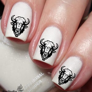 May include: Three white fingernails with black buffalo head nail art decals. The buffalo head is facing forward with a black outline and a white interior.