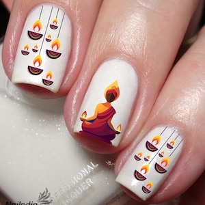 以下が含まれることがあります： 白いマニキュアに、ろうそくを灯した瞑想する人のデザインと、他の爪にぶら下がっているろうそくの灯りのデザインが施されています。