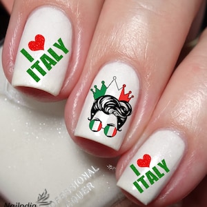 Puede incluir: Esmalte de uñas blanco con calcomanías de arte de uñas verdes y rojas. Las calcomanías muestran las palabras "Me encanta Italia" con un corazón rojo, una corona y una imagen de dibujos animados de una persona con gafas de sol con los colores de la bandera italiana.