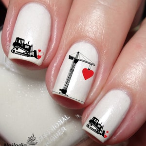 Pode incluir: Esmalte de unha branco com desenhos de arte de unha pretos e vermelhos. Uma unha tem uma grua com um coração vermelho, outra tem uma escavadora com dois corações vermelhos e outra tem uma escavadora com um coração vermelho.
