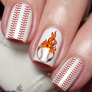 Op de afbeelding: Witte nagellak met rode baseballsteekontwerpen en een witte baseball met rode steken en oranje vlammen op één nagel.