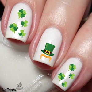 May include: White nail polish with green shamrock and leprechaun hat nail art decals.