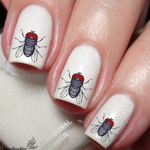 May include: White nail polish with fly nail art. Each nail features a cartoon fly design with red eyes, gray body, and black wings. The image includes the text "Nailodia" and "Proudly Designed and Produced in Australia".