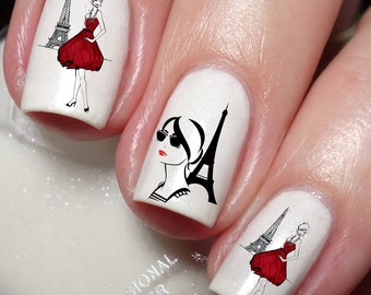 May include: White nail polish with black and red nail art featuring a woman in a red dress and the Eiffel Tower.