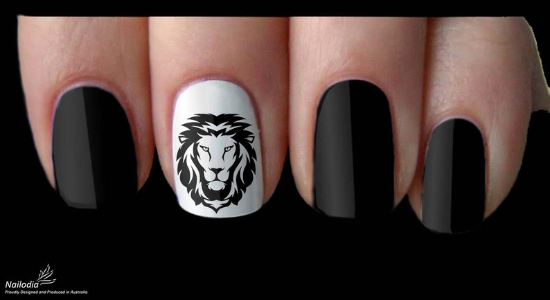 May include: Black and white lion head nail art design on a white nail polish background. The design is on a finger with black nail polish on the other fingers.