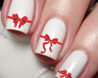 May include: White nail polish with red bow nail art designs. The nail art features a red ribbon with a bow on each nail.