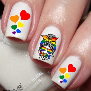 May include: White fingernails with rainbow heart designs and one nail with a rainbow-themed design that says "Pride Mom".