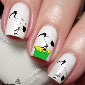 May include: White nail polish with black and white drawings of an Australian Ibis bird on three fingernails. One fingernail has a drawing of the bird standing on a green and yellow trash can.