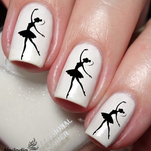 May include: Three white fingernails with black silhouette images of ballerinas. The nail polish is a pearlescent white with a shimmery finish. The image is a close-up of the fingernails.