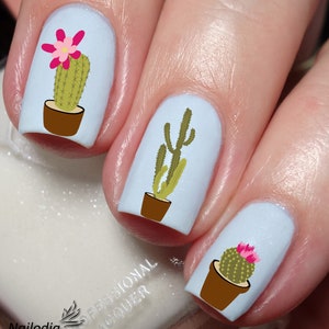 Può includere: Tre unghie con smalto per unghie blu chiaro e adesivi per nail art a forma di cactus. Gli adesivi raffigurano cactus verdi con fiori rosa in vasi marroni.