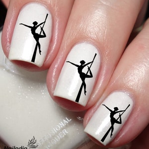 May include: White nail polish with black silhouette nail art decals of a person on a pole. The decals are on three fingernails.
