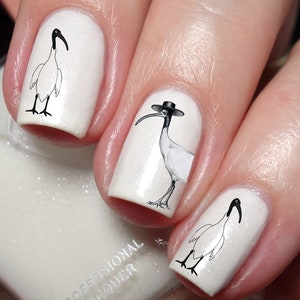 May include: White nail polish with black and white ibis bird nail art decals. The ibis birds are wearing hats.