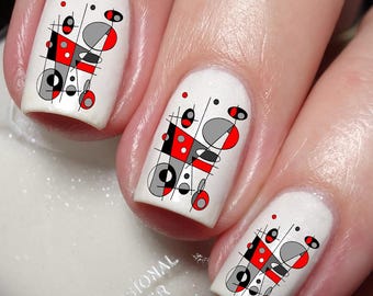 May include: Close-up of five fingernails with white nail polish and abstract geometric nail art decals in black, red, and gray.