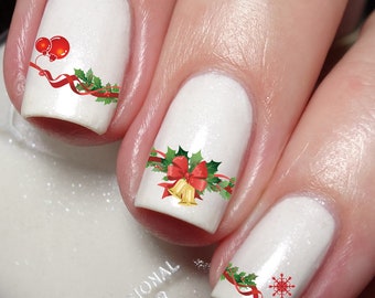 May include: White nail polish base with festive holiday nail art decals. One nail features red ornaments and holly, another shows gold bells with a red bow and holly, and the third displays a red snowflake with a red ribbon and holly.