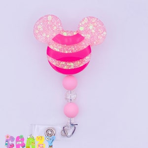 May include: Pink and white glitter mouse ear shaped badge reel with a pink and white striped center. The reel has a clear badge holder and a pink and white beaded chain.