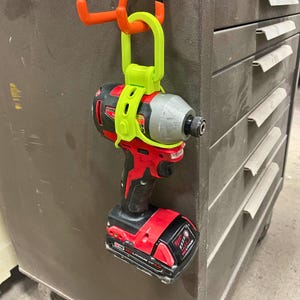 May include: A bright yellow plastic tool holder with a hook for hanging a red and black power drill. The drill has a black and silver drill bit and a red battery pack that says "18V RED LITHIUM CP 2.0".