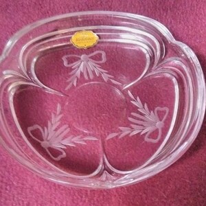 Puede incluir: Un cuenco de vidrio transparente con un diseño grabado decorativo de lazos y hojas. El cuenco tiene un borde elevado y está hecho por la empresa "Black Forest Crystal".