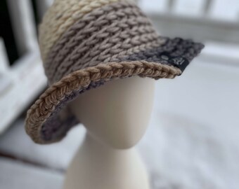 May include: A crocheted hat with a brown, beige, and gray striped pattern. The hat has a wide brim and is made with a chunky yarn.