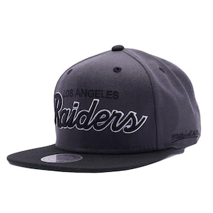 May include: A charcoal gray and black Los Angeles Raiders baseball cap. The cap features the team name in white script across the front and the text "LOS ANGELES" above it. The brim is black.