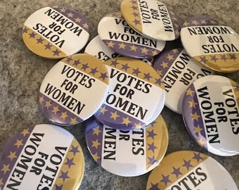 Puede incluir: Un conjunto de botones redondos con el texto "VOTES FOR WOMEN" en blanco sobre un fondo morado y dorado. Los botones presentan un diseño de estrellas y están dispersos sobre una superficie texturizada.
