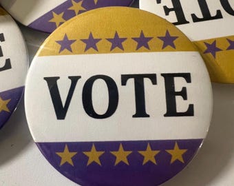 May include: A collection of round buttons with the word "VOTE" in bold black letters. The buttons have a white center with a purple and gold border, and gold star accents. The buttons are for political campaigns.