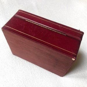 May include: A burgundy velvet box with a gold trim and a brass hinge. The box is closed.