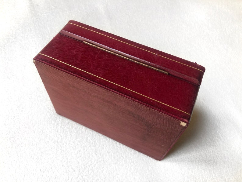 May include: A burgundy velvet box with a gold trim and a brass hinge. The box is closed.