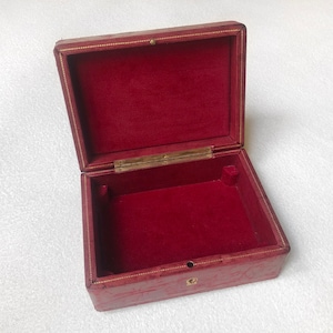 May include: A red leather box with a gold trim and a red velvet interior. The box is open and empty.