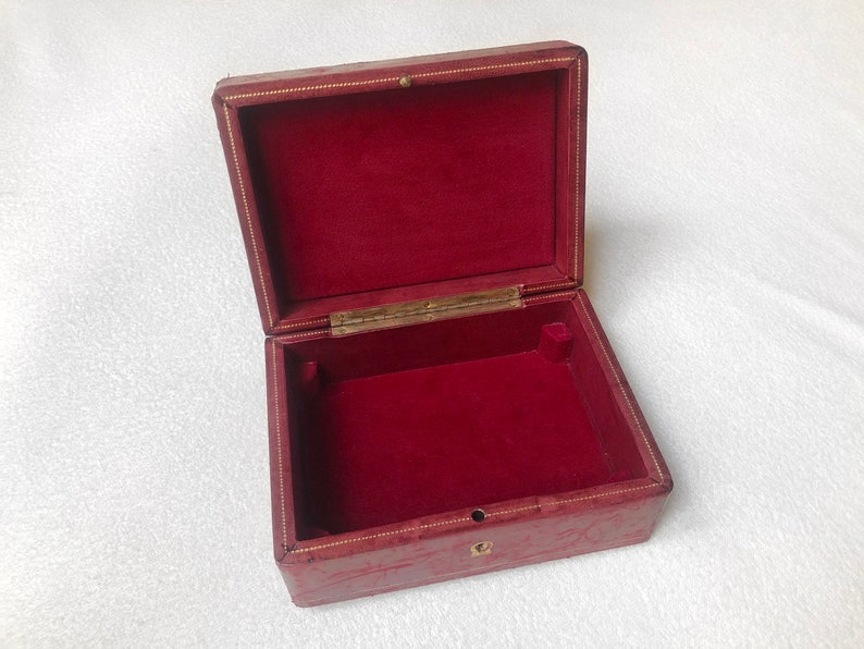 May include: A red leather box with a gold trim and a red velvet interior. The box is open and empty.