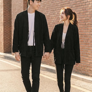 May include: A couple walking down a street, both wearing black outfits. The outfits include black jackets, pants, and shoes. The man is wearing a white t-shirt, and the woman is wearing a white top. They are holding hands.